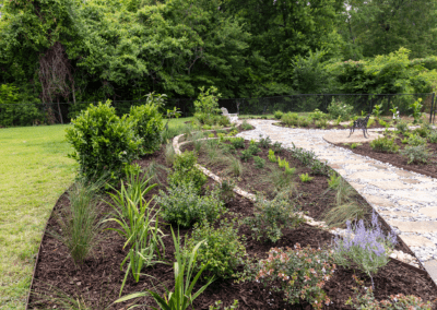 Finished backyard project. Photo of a flower bed with lush plants and a flagstone path to the right.