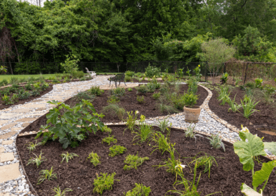 Finished backyard landscape project with visible tan flagstone pathways, rock borders, and lush green plants.